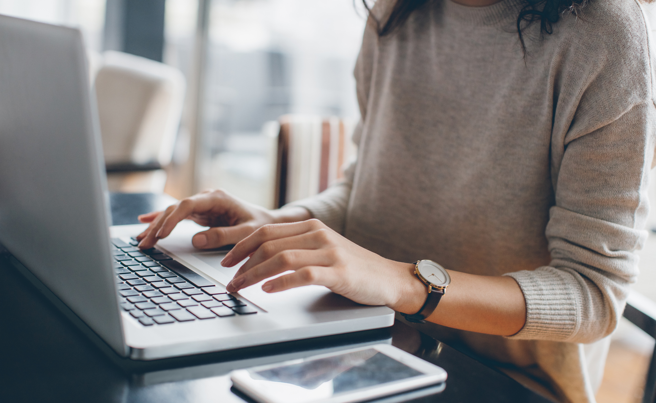 Woman sitting at desk, it can be inferred that she is writing for a blog on her laptop